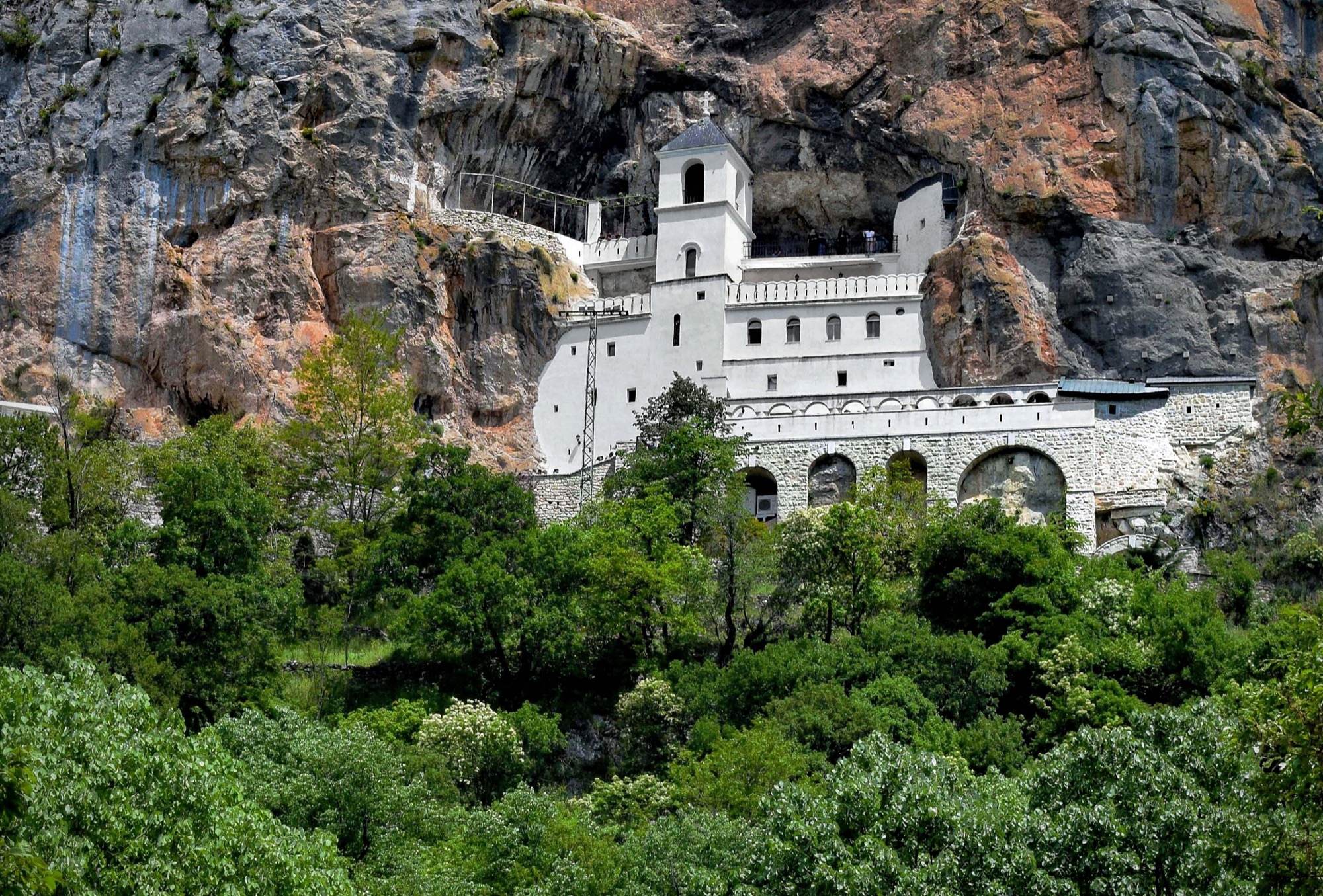 The white Upper Monastery of Ostrog built into a vertical cliff above green woods